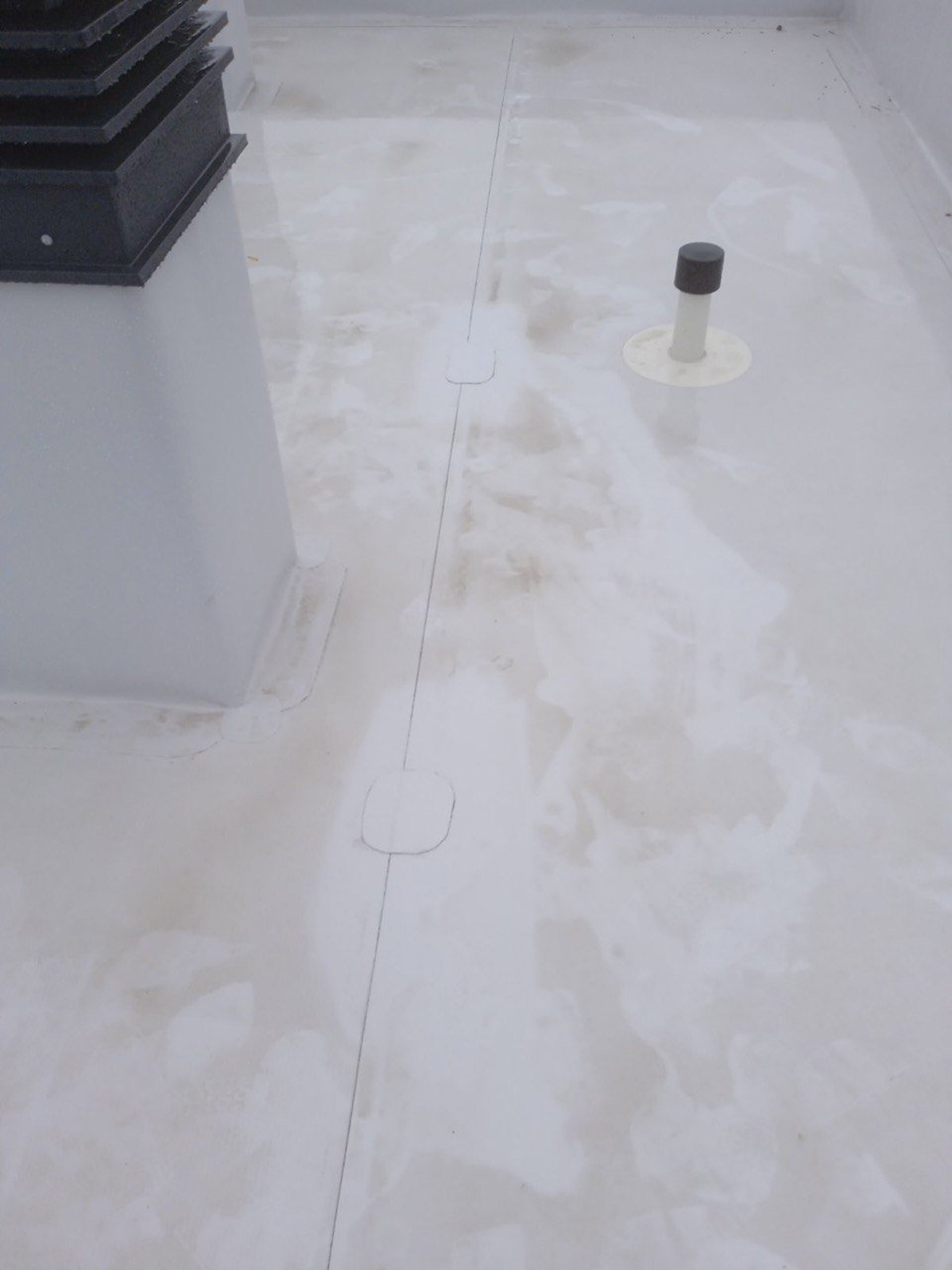 A flat white rooftop with a vent pipe, a rectangular structure, and visible seams on the surface.