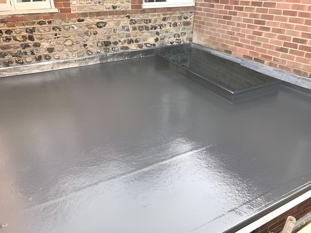 Flat roof with a smooth, shiny waterproof surface, adjacent to brick and stone walls, featuring a rectangular rooflight window.