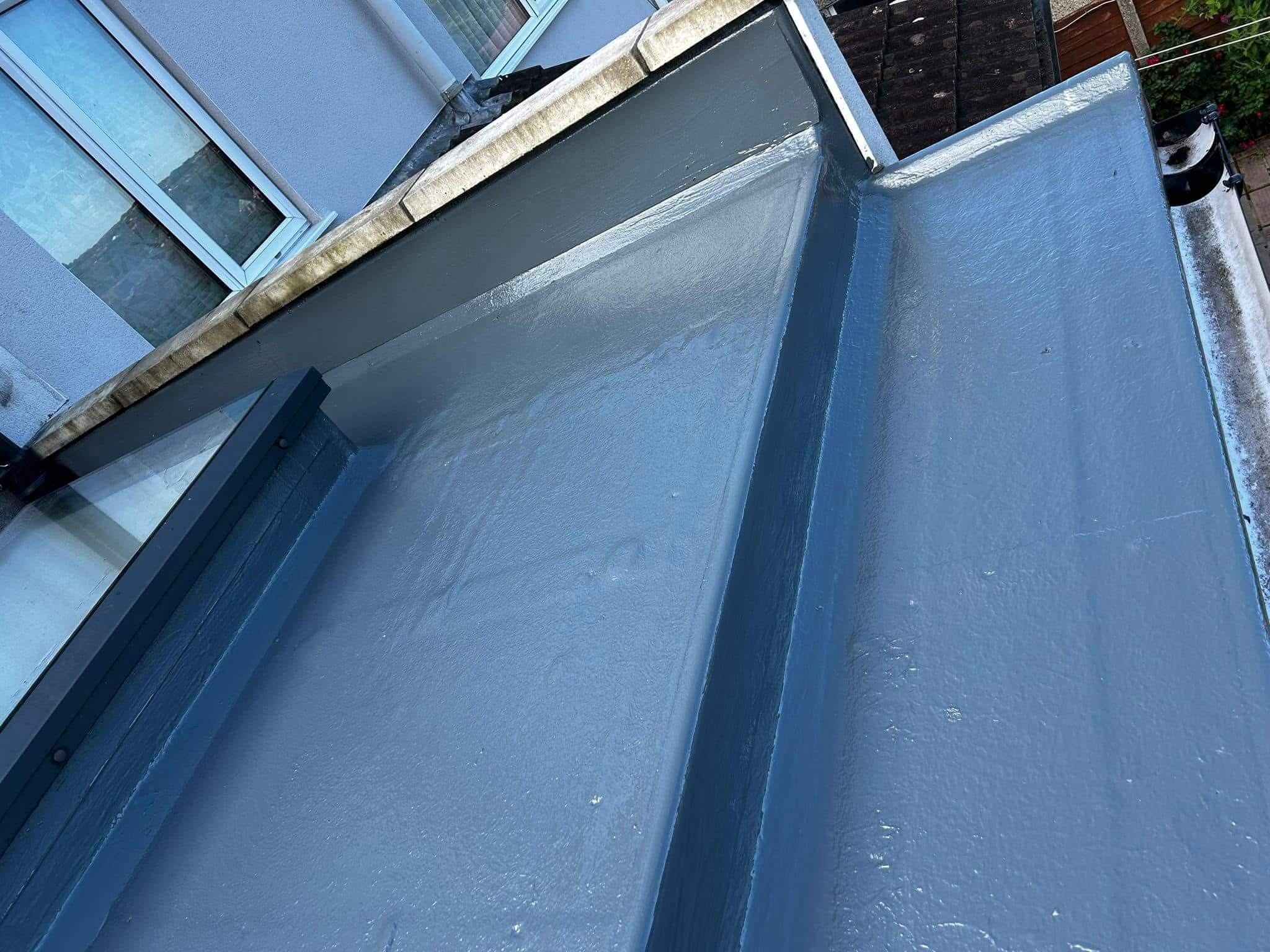 A freshly painted flat roof with grey waterproof coating outside a building, adjacent to windows and a wooden fence.